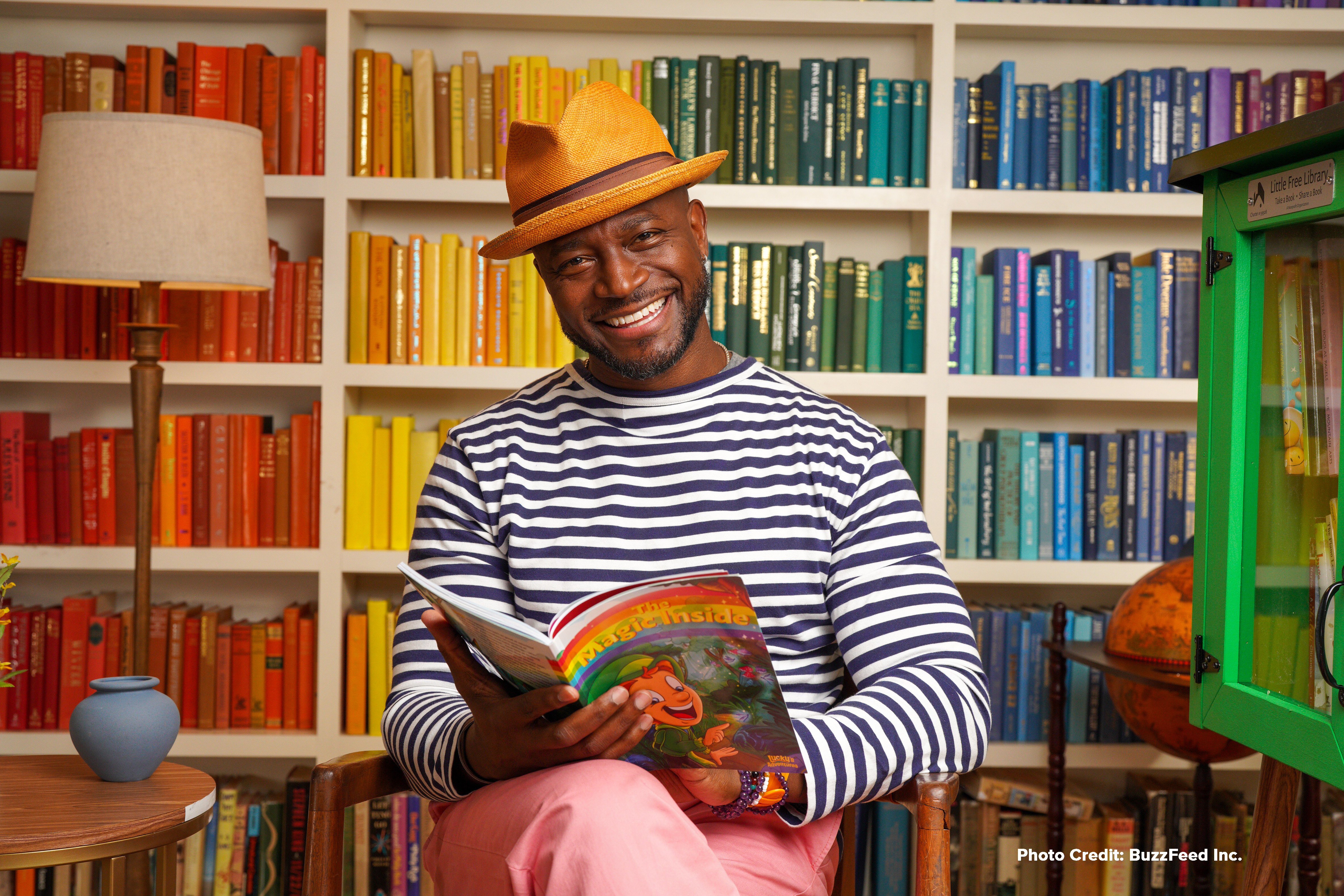 Taye Diggs holding The Magic Inside book in front of a rainbow bookshelf